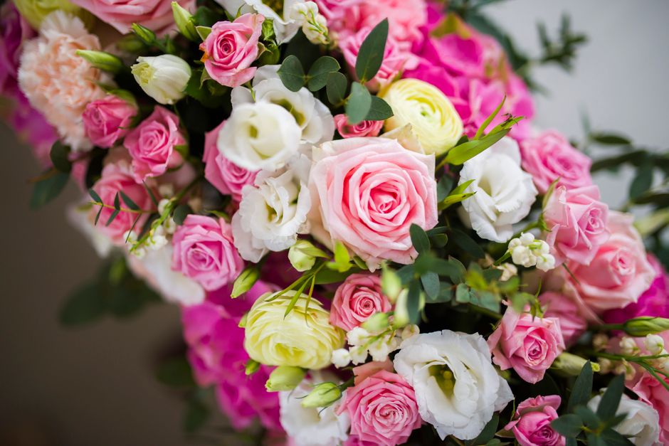 A close-up of a floral bouquet featuring a variety of fresh flowers, predominantly in shades of pink, white, and cream. The arrangement includes large pink roses, white lisianthus, and smaller pink sp